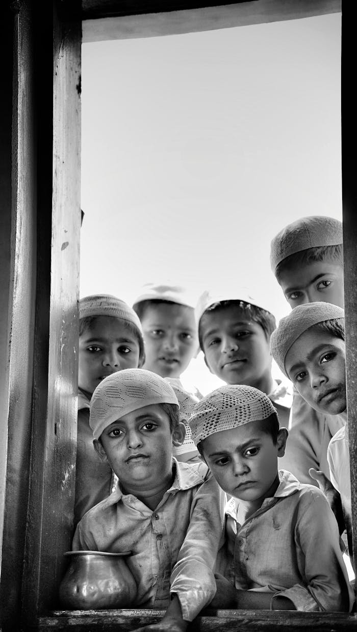 who-we-are A group of children in traditional attire gazing through a window with solemn expressions.