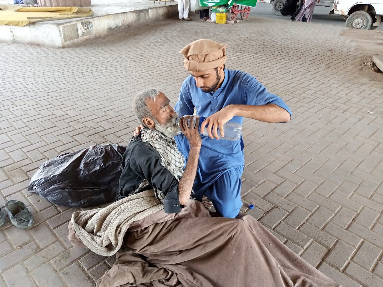 about-us A young man helps a homeless senior by giving water outdoors in Karachi, Pakistan.
