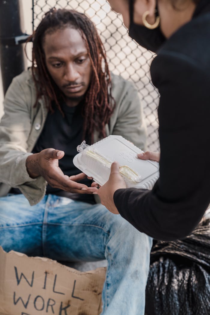 services-01 A person with dreadlocks receiving a meal from a helping hand on the street, showcasing kindness.